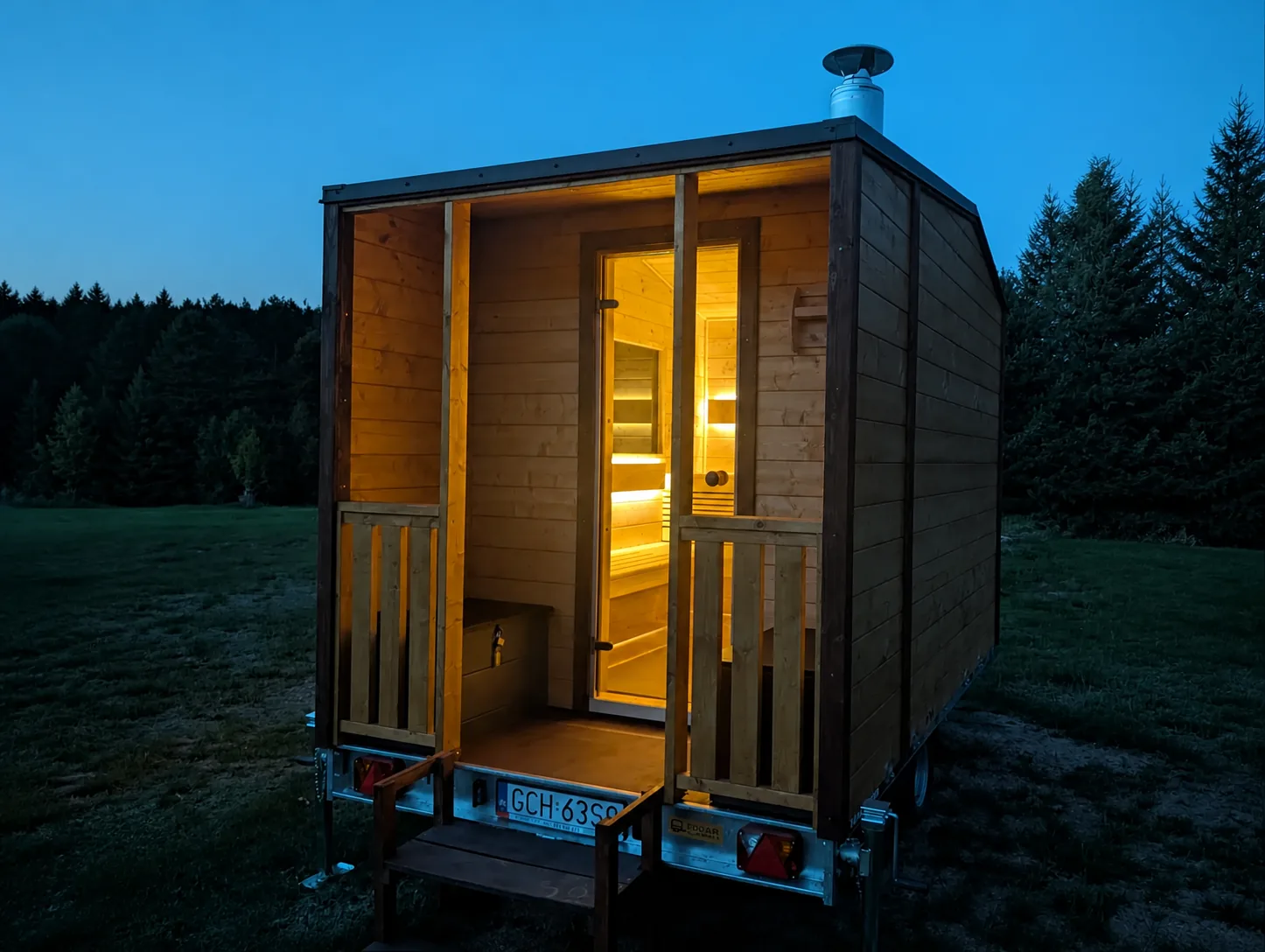 Oświetlona sauna mobilna na lawecie na tle trawnika i drzew